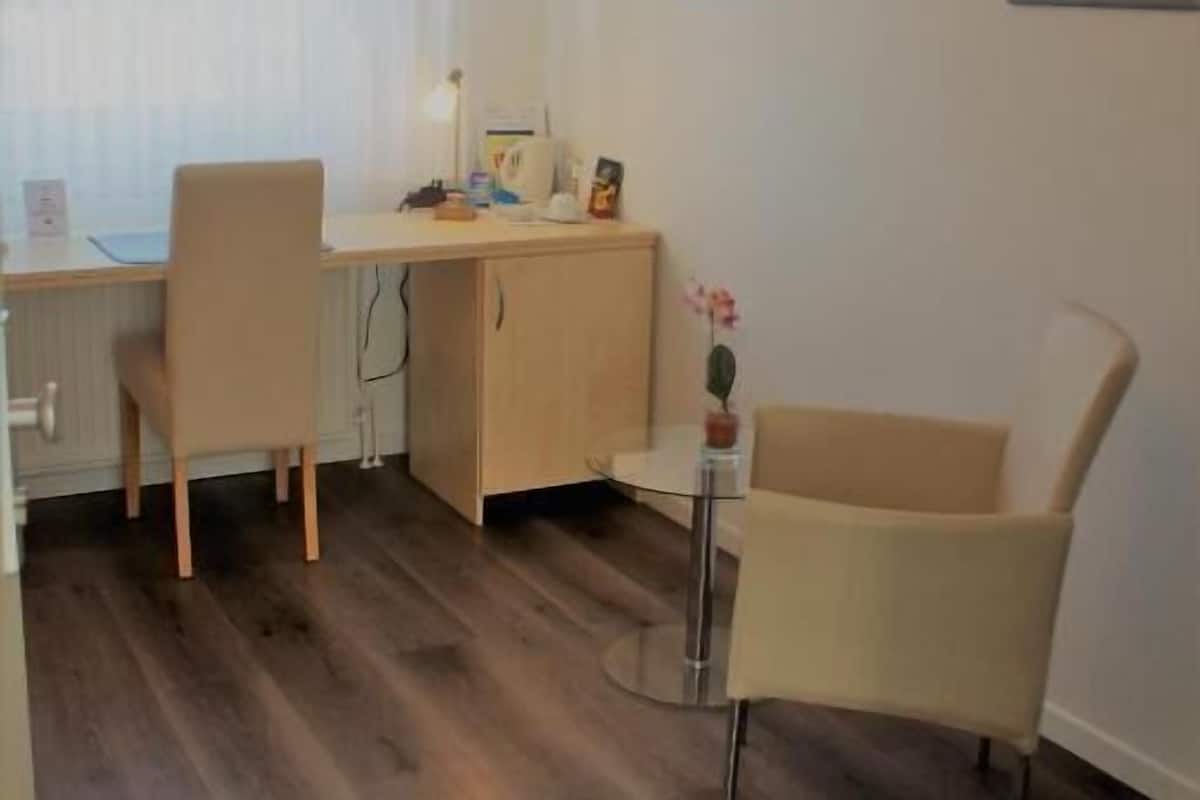 Una habitació amb un escriptori de fusta, dues cadires, una taula petita amb un ram i un armari.