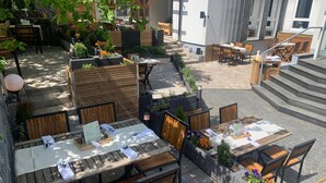 An outdoor patio area with wooden tables and chairs, stone flooring, and potted plants. - Hotel-Restaurant Zum Schwanen (Wermelskirchen)