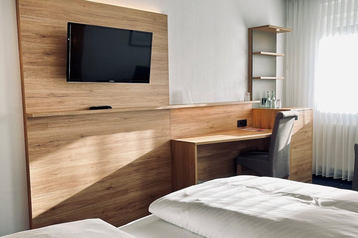 Habitació d'hotel amb escriptori de fusta, televisió de pantalla plana, llit i finestra amb cortines primes.