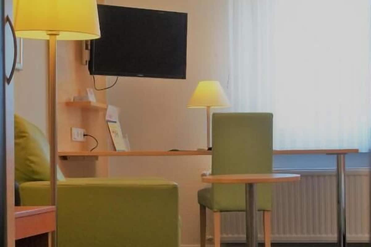 Una habitació amb un sofà verd, una taula petita, una làmpada i una televisió.