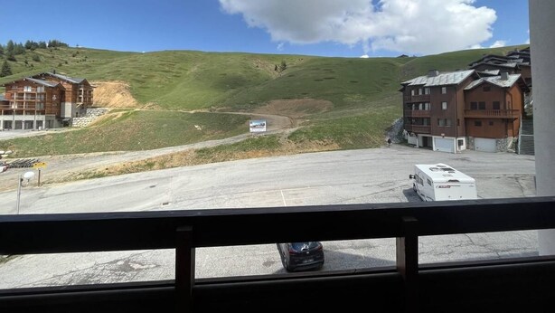 A view from inside a building looking out to a parking area with a building and a hill in the background.