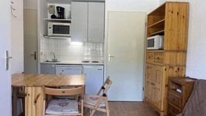 A compact kitchen with white cabinets, a microwave, and a coffee maker. There's a wooden dining table with chairs and a wooden cabinet with shelves.