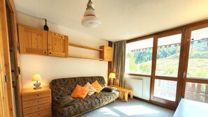 A cozy room with a sofa, wooden cabinets, a table, and a window with a view of greenery.