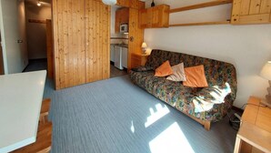 A compact room with a sofa, a small table, a kitchenette, and a ceiling fan.