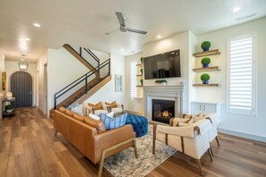 A modern living room with a fireplace, a staircase, and a flat-screen TV.