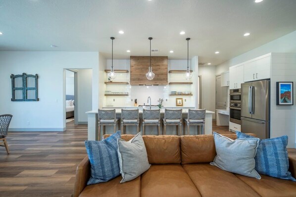 A modern kitchen with a central island, pendant lighting, and a dining area with chairs.