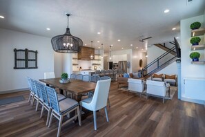 A spacious living area with a wooden dining table, light-colored chairs, a sofa, and a staircase. - Steps to Pool + Pickleball | 2 Fire Pits | Arcade Game | Arcadia #15 (Santa Clara)
