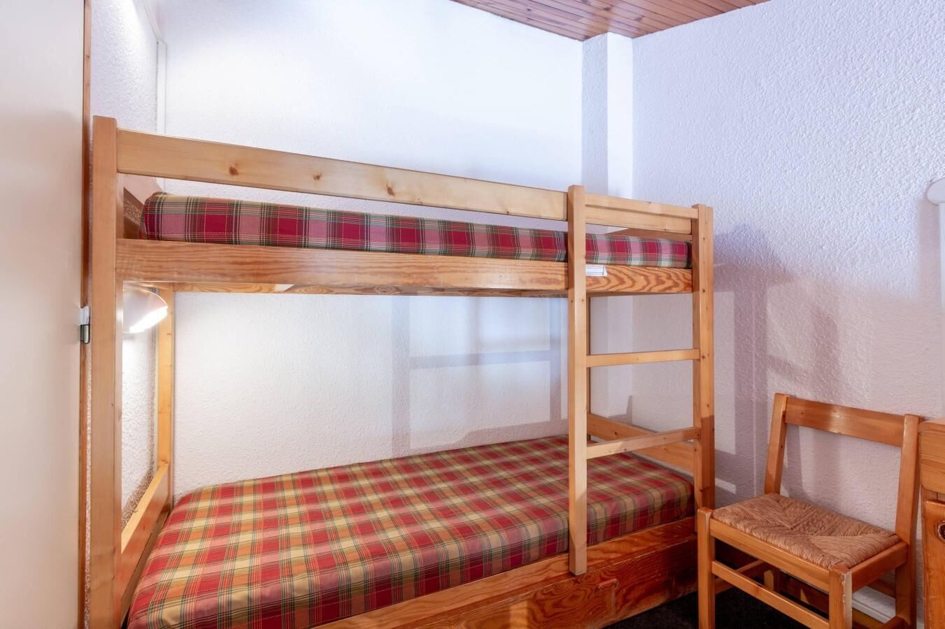 A bunk bed with a plaid mattress and a wooden chair.