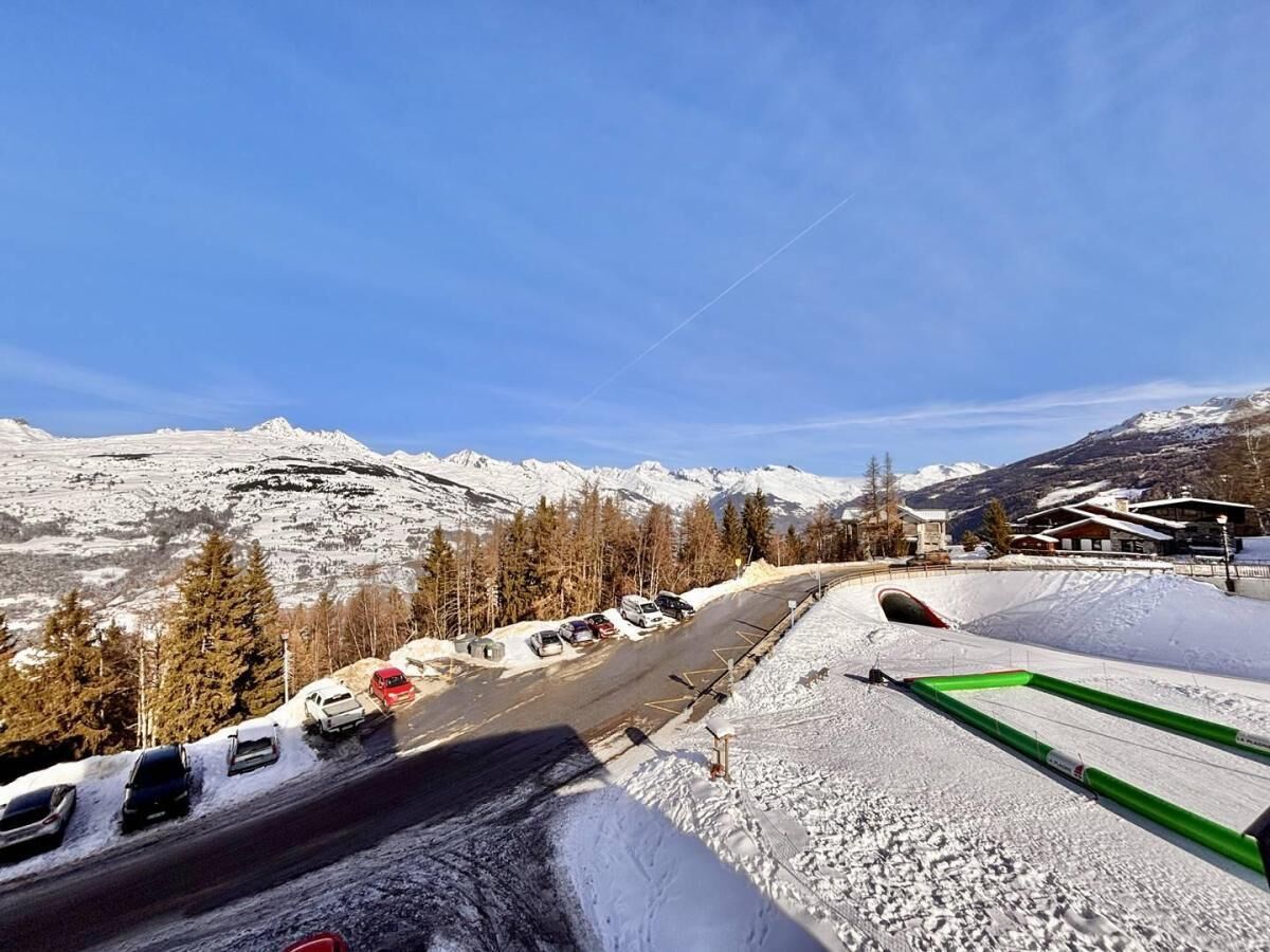 A snowy mountain road with parked cars and a ski lift.