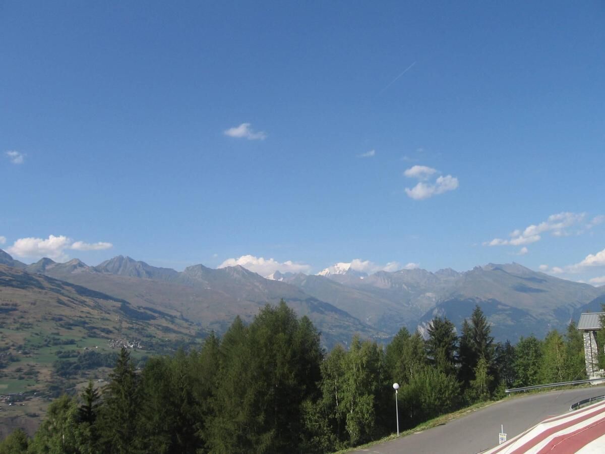 A road with a mountain view, a stone building, and a clear sky.