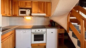 Una cucina compatta con mobili in legno, un forno a microonde, un piano cottura, una lavastoviglie e un piccolo frigorifero.