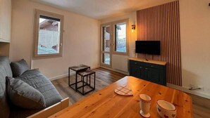 A modern living room with a sofa, a wooden dining table with cups, a TV on the wall, and a window. - 300m from resort center, view mountain, terrace, tv, ski locker, 20m², Montchavin La Plagne (Bellentre)