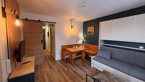 A cozy living room with a wooden dining table, a gray sofa, and a TV on a wooden stand. - 300m from resort center, view mountain, terrace, tv, ski locker, 20m², Montchavin La Plagne (Bellentre)