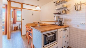 A compact kitchen with a built-in oven, a coffee maker, and a wooden dining area with chairs. - 50m from ski slopes, 2nd floor, view mountain, balcony, tv, ski locker, 27m², Montchavin La Plagne (Bellentre)