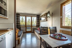 Enjoy a cozy space with a kitchenette, large window, and seating area, perfect for dining or socializing amidst the surrounding forest.