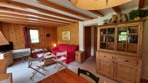 A cozy cabin with wooden walls and ceilings, a red sofa, a wooden cabinet, and a dining table with chairs. - Balcony, tv, 65m², Méribel-Mottaret (Méribel - Les Allues)