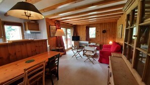 A cozy cabin interior with a wooden dining table, chairs, a red sofa, and a television. - Balcony, tv, 65m², Méribel-Mottaret (Méribel - Les Allues)