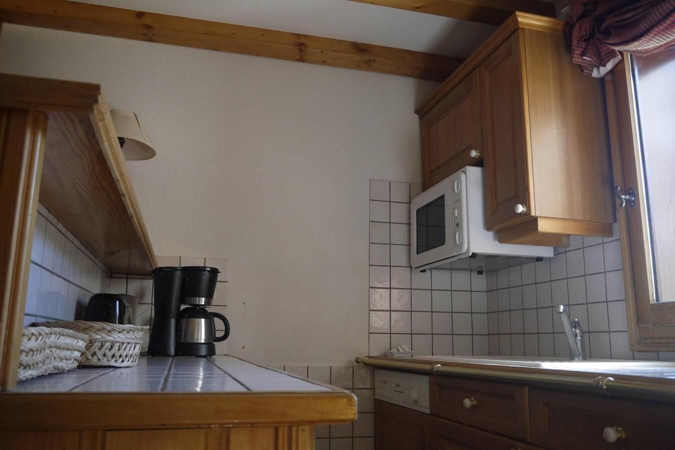 Una cucina con mobili in legno, un forno a microonde, una macchina da caffè e uno schienale piastrellato.