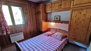A wooden cabin bedroom with a checkered bedspread, a radiator, and wooden cabinets. - Balcony, tv, 65m², Méribel-Mottaret (Méribel - Les Allues)