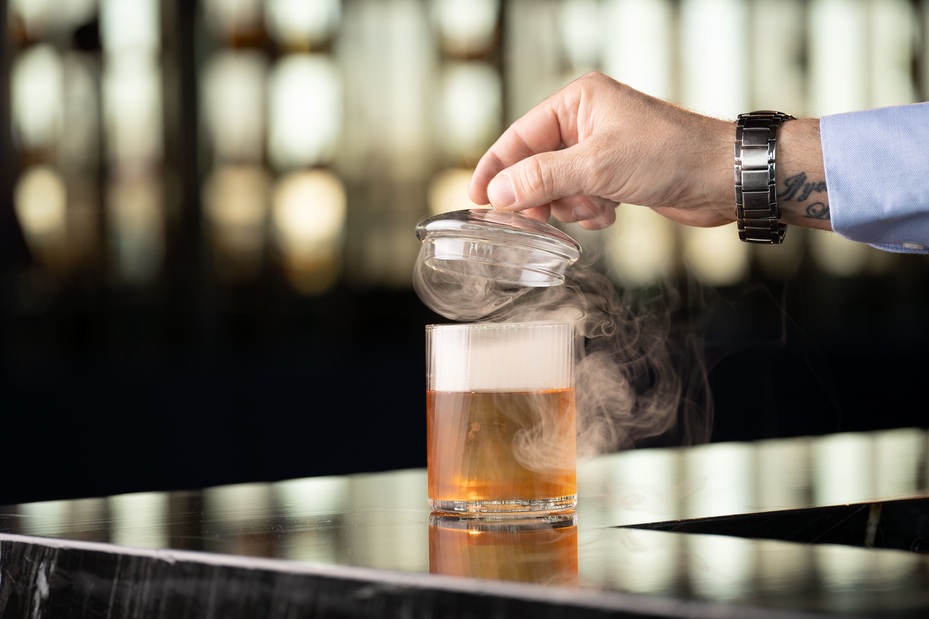 Eine Hand gießt ein Getränk in ein Glas, Dampf steigt daraus auf.