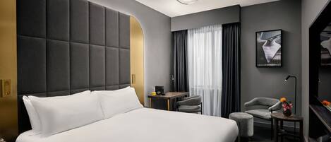 Quarto de hotel moderno com uma cama grande, uma escrivaninha, uma cadeira e uma pequena mesa com flores.