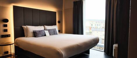 Una habitación de hotel moderna con una cama grande, una lámpara de techo redonda y vistas de la ciudad a través de la ventana.