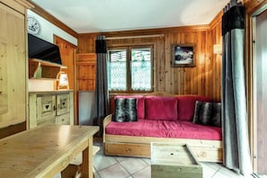 Um quarto acolhedor estilo cabana, com decoração em madeira, um sofá com almofadas vermelhas, uma mesa de madeira e uma janela com cortinas.