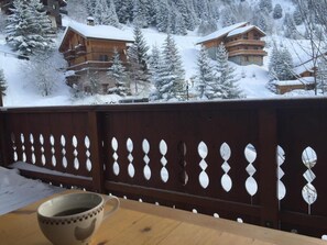 A wooden deck with a table and a cup, overlooking a snow-covered mountain area with buildings.