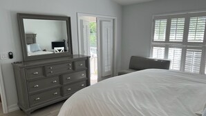 Ein Schlafzimmer mit einem großen Bett, einem Schminktisch, einem Spiegel und einem Fenster mit Jalousien.