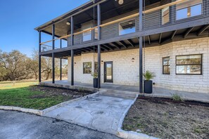 A modern two-story building with a brick facade, large windows, and a covered outdoor area with potted plants. - EcoView Villa•Pool•Spa•Goats•85 acres•Amazing view (Austin)