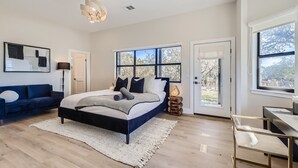Ein Schlafzimmer mit einem Bett, einem Schreibtisch, einem Sessel, einer Couch und einem großen Fenster.
