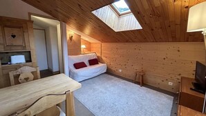 Ein gemütliches Schlafzimmer im Dachgeschoss mit einem Oberlicht, einem Schlafsofa, einem Esstisch und einem Fernseher.