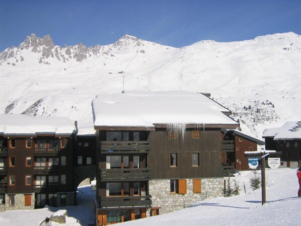 A multi-story hotel with a stone facade and wooden balconies, set against a snowy mountain backdrop. - 20m from ski slopes, 4th floor, view building, 13m², Méribel-Mottaret (Méribel - Les Allues)