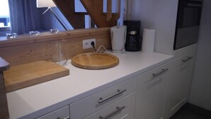 A kitchen with a wooden cutting board, a coffee maker, and a sink.
