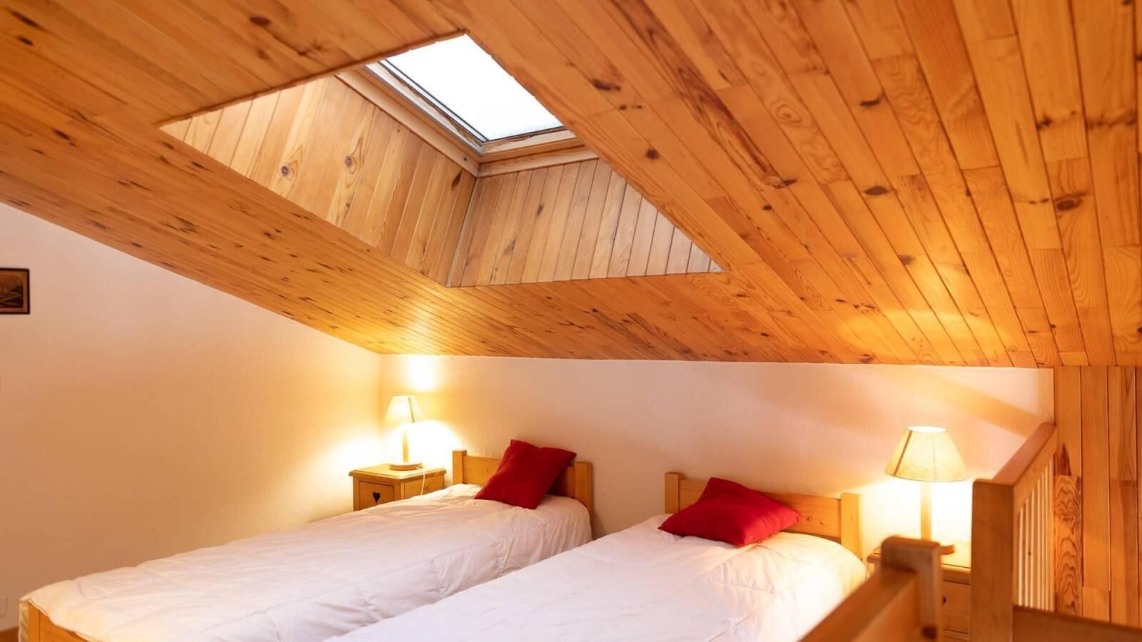 A bedroom with two beds, wooden ceiling beams, and a skylight.