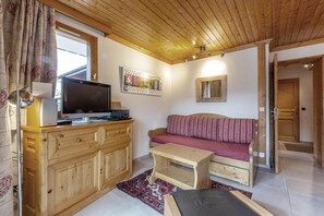 Una habitación acogedora con techo de madera, un televisor sobre un mueble de madera, un sofá estampado y una pequeña mesa de madera.