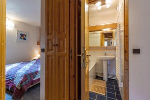 Quarto com cama, porta de madeira, banheiro com pia e espelho, e piso revestido de azulejos.