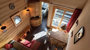 A cozy cabin interior with a dining area, a sofa, and a small kitchen visible through an open door.