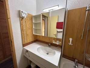 Une salle de bain avec un lavabo blanc, un meuble-lavabo en bois, un miroir, un porte-serviettes et une douche.