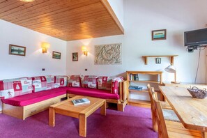 A cozy living room with a wooden ceiling, a sectional sofa with patterned cushions, a coffee table, a dining table with chairs, and a flat-screen TV mounted on the wall. - 180m from shops, floor -1, view mountain, balcony, 60m², Méribel-Mottaret (Méribel - Les Allues)