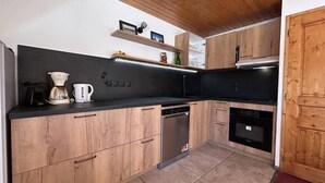 A kitchen with wooden cabinets, a dishwasher, a coffee maker, and a stove. - 180m from shops, floor -1, view mountain, balcony, 60m², Méribel-Mottaret (Méribel - Les Allues)