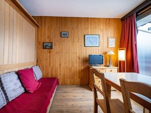 Una habitación con paneles de madera, un sofá rojo, un televisor y una mesa con sillas.