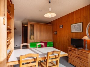 Ein Zimmer mit einem Holztisch, Stühlen, einem Fernseher und einem Schrank.