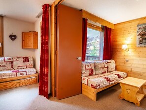 Quarto aconchegante com decoração em madeira, cama com roupa de cama estampada, uma mesinha e janela com cortinas.