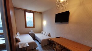 A room with two beds, a wooden table, and a TV mounted on the wall. - 50m from ski slopes, 2nd floor, balcony, tv, 28m², Méribel-Mottaret (Méribel - Les Allues)