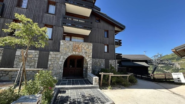A modern building with a stone facade, wooden balconies, and a ski lift in the background. - 50m from ski slopes, 2nd floor, balcony, tv, 28m², Méribel-Mottaret (Méribel - Les Allues)