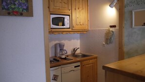 A compact kitchen with wooden cabinets, a microwave, a coffee maker, and a dishwasher. - 10m from ski slopes, floor -1, view ski slopes, balcony, 32m², Méribel-Mottaret (Méribel - Les Allues)