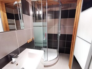 A modern bathroom with a glass-enclosed shower, a white sink, and a wooden ceiling.