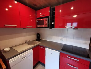 A compact kitchen with red cabinetry, a microwave, a dishwasher, and a sink. - 10m from ski slopes, 1st floor, view ski slopes, balcony, 32m², Méribel-Mottaret (Méribel - Les Allues)