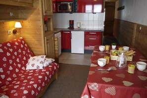 A cozy room with a bed, a dining table set with cups and a basket of bread, and a kitchen with red cabinets and a microwave. - 10m from ski slopes, 1st floor, view ski slopes, balcony, 32m², Méribel-Mottaret (Méribel - Les Allues)